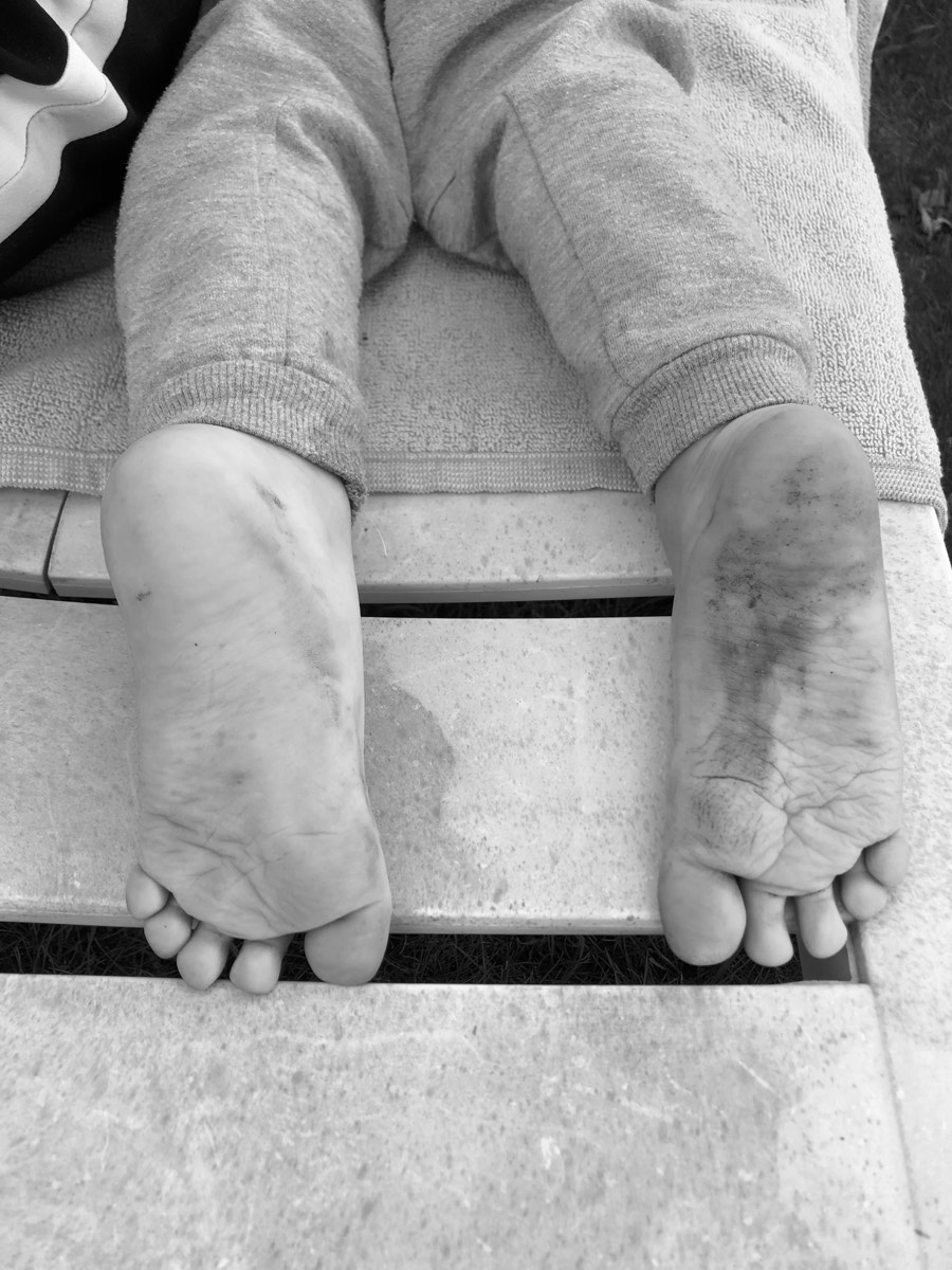 Os pés descalços e sujos de uma criança, num banco de jardim