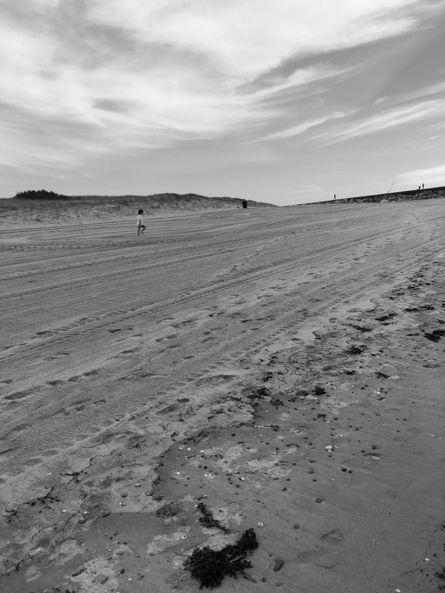 Uma criança pequena a correr numa praia larga, com o horizonte ao fundo